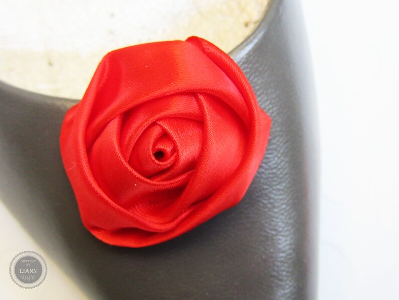 Pu&ograve; includere: Un fiocco di fiore di rosa in raso rosso brillante. La rosa &egrave; fatta di tessuto ed &egrave; un unico fiore.