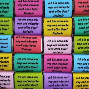 Könnte beinhalten: Eine Sammlung rechteckiger Schokoladentafeln, eingewickelt in buntes Papier in den Farben Grün, Pink, Blau, Gelb, Lila und Rot. Jede Verpackung trägt den schwarzen Aufdruck: Ich bin dann mal weg und wünsche euch alles Gute! Stefanie.