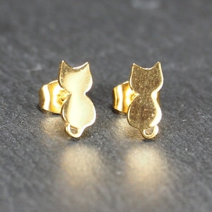 Puede incluir: Un par de pendientes de botón de oro en forma de gato. Los pendientes son pequeños y delicados, y serían un gran regalo para un amante de los gatos.
