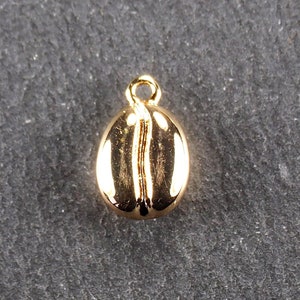 Op de afbeelding: Een gouden koffieboon charme hanger. De charme is gevormd als een koffieboon en heeft een kleine lus aan de bovenkant om aan een ketting of armband te bevestigen.
