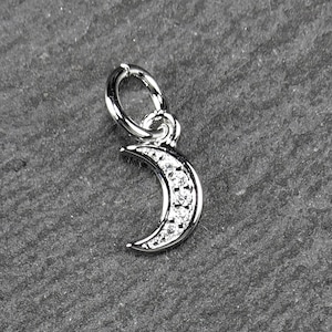 Peut inclure: Un charme en argent en forme de croissant de lune avec de petits cristaux transparents autour du bord. Le charme a un anneau de saut pour l'attacher à un bracelet ou un collier.