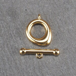 May include: Gold-toned metal clasp with a round, open loop and a straight bar with rounded ends. The clasp is used for jewelry making.