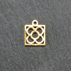 Pode incluir: Encanto de metal dourado com forma quadrada e um design geométrico de círculos sobrepostos.