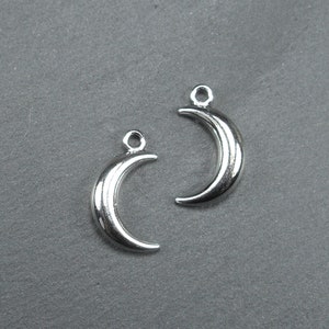 Könnte beinhalten: Zwei silberne Halbmond-Anhänger mit einer Öse oben zum Anbringen an Schmuck oder andere Bastelarbeiten.