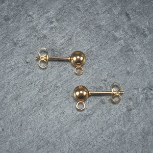 Könnte beinhalten: Zwei goldfarbene Ohrring-Verschlüsse mit einer runden Kugel am Ende und einer Öse zum Anbringen von Schmuck.