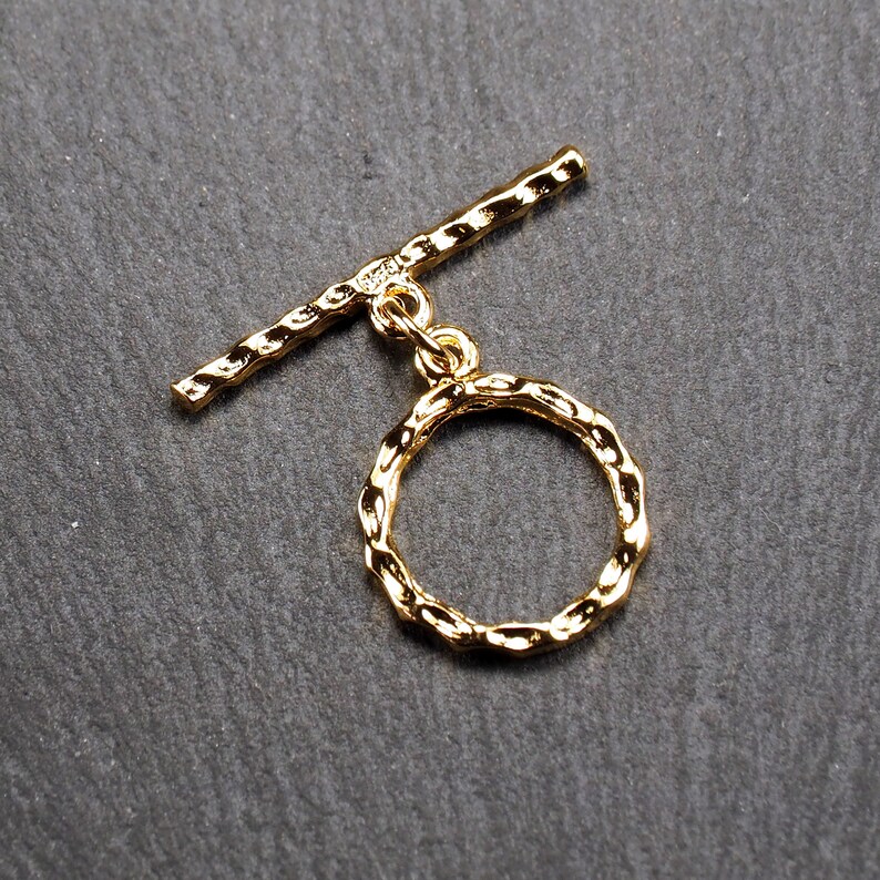 May include: Gold-toned metal toggle clasp with a textured, round ring. The clasp is designed for jewellery making and features a sturdy, secure closure.
