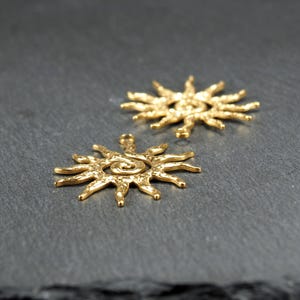 May include: Two gold-toned metal sun charms with a spiral design in the center. The charms have a textured surface and are perfect for jewelry making.
