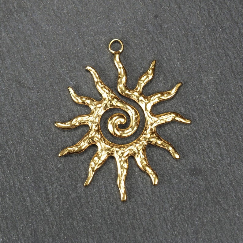 May include: Gold-toned metal sun pendant with a spiral design in the center. The sun has a textured surface and a loop at the top for hanging.