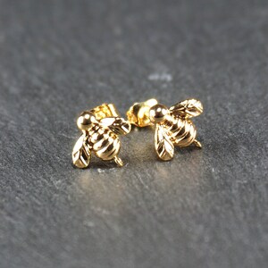 May include: A pair of gold bee stud earrings. The bees are detailed and have a realistic appearance.