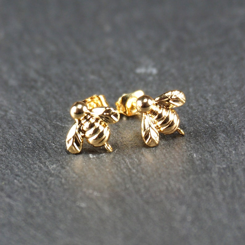 May include: A pair of gold bee stud earrings. The bees are detailed and have a realistic appearance.