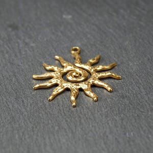 May include: Gold-toned metal sun pendant with a spiral design in the center. The sun has a textured surface and a loop at the top for hanging.