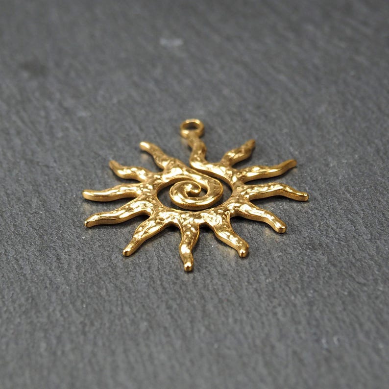 May include: Gold-toned metal sun pendant with a spiral design in the center. The sun has a textured surface and a loop at the top for hanging.