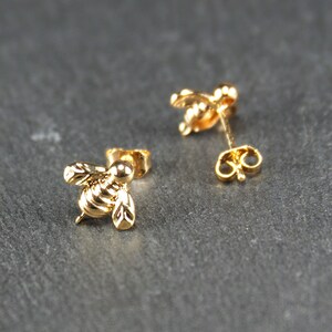 May include: A pair of gold bee stud earrings. The bee is detailed with wings and a body.