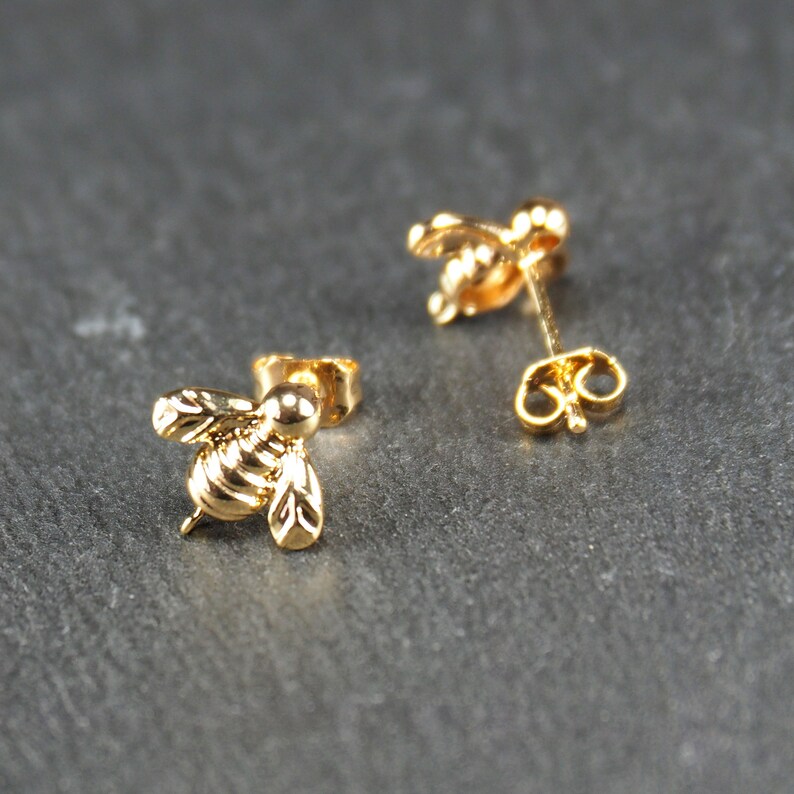 May include: A pair of gold bee stud earrings. The bee is detailed with wings and a body.