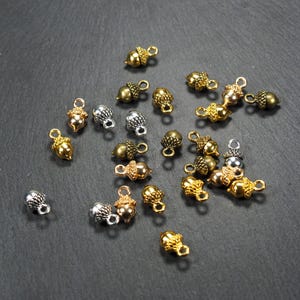 Puede incluir: Una colección de abalorios de bellota de oro, plata y bronce con un bucle para sujetar a joyas u otras manualidades.