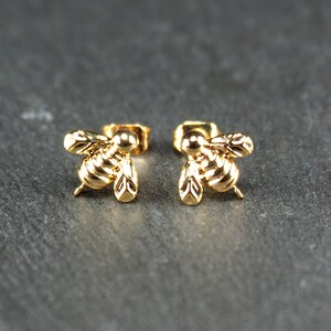 May include: A pair of gold bee stud earrings. The bees are detailed and have a three-dimensional look.