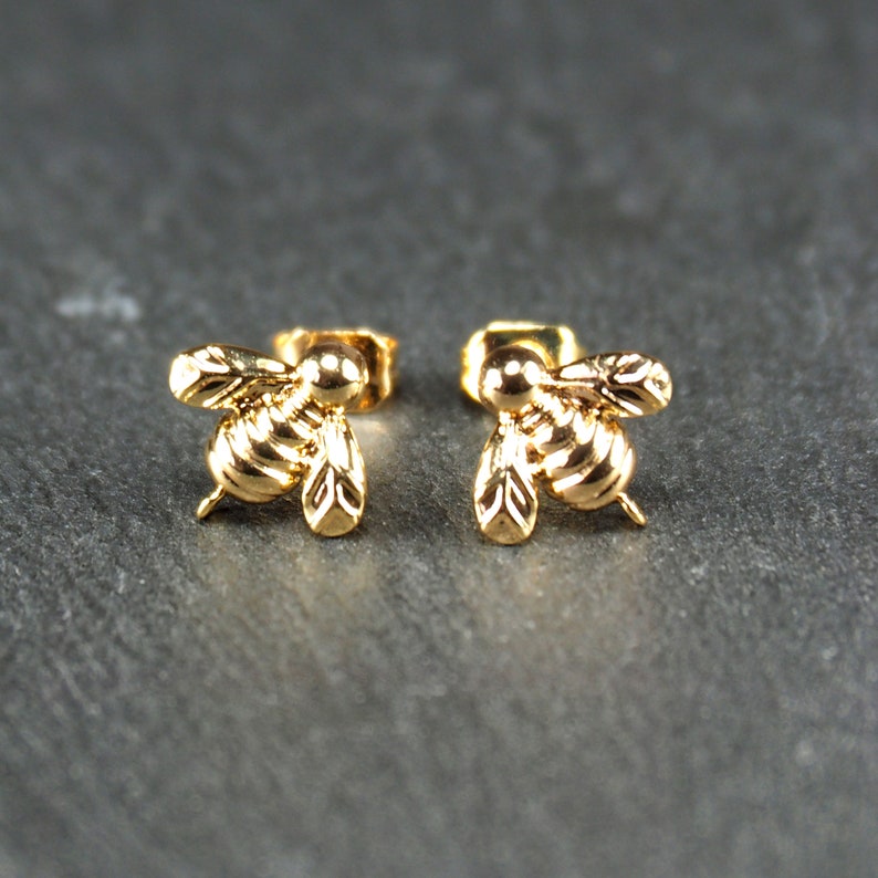 May include: A pair of gold bee stud earrings. The bees are detailed and have a three-dimensional look.