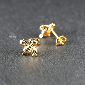 May include: A pair of gold bee stud earrings. The bee is detailed with wings and a segmented body.