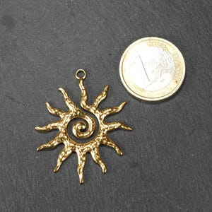 May include: Gold-toned metal sun pendant with a spiral design. The pendant has a textured surface and a loop at the top for attaching to a chain or cord.