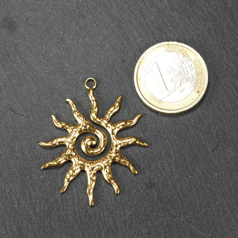 May include: Gold-toned metal sun pendant with a spiral design. The pendant has a textured surface and a loop at the top for attaching to a chain or cord.