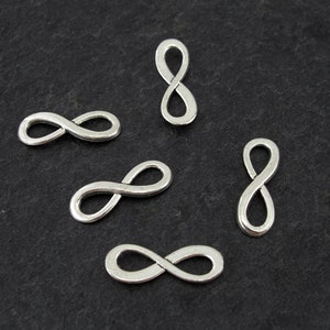 Könnte beinhalten: Fünf silberne Unendlichkeits-Anhänger auf schwarzem Hintergrund. Die Anhänger sind etwa 2,5 cm lang.