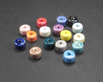 Puede incluir: Surtido de 16 cuentas de cerámica en forma de donut en varios colores, incluyendo azul, verde, amarillo, rojo, naranja, rosa y blanco. Las cuentas son todas del mismo tamaño y forma, y están dispuestas en círculo sobre una superficie negra.