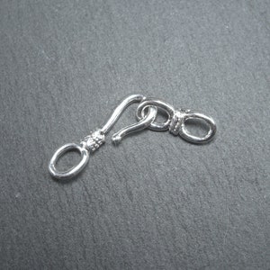 May include: Silver-toned metal clasp with a hook and loop closure. The clasp is designed for attaching jewellery or other items.