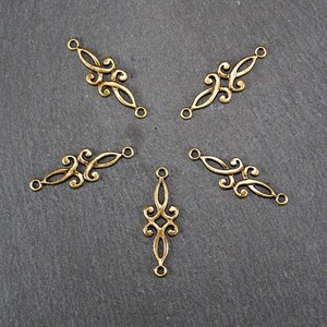 Puede incluir: Cinco conectores decorativos de metal dorado con intrincados dise&ntilde;os de volutas. Los conectores tienen dos agujeros cada uno para sujetar a joyas u otras artesan&iacute;as.