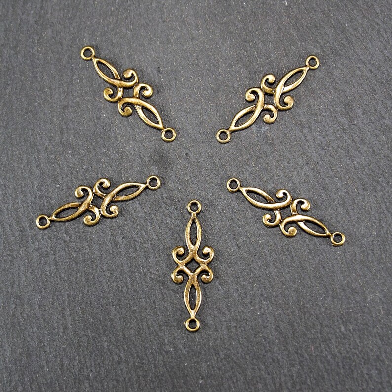 Puede incluir: Cinco conectores decorativos de metal dorado con intrincados dise&ntilde;os de volutas. Los conectores tienen dos agujeros cada uno para sujetar a joyas u otras artesan&iacute;as.