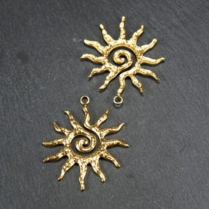 May include: Two gold-toned metal sun charms with a spiral design in the center. Each charm has a loop at the top for attaching to jewelry or other crafts.