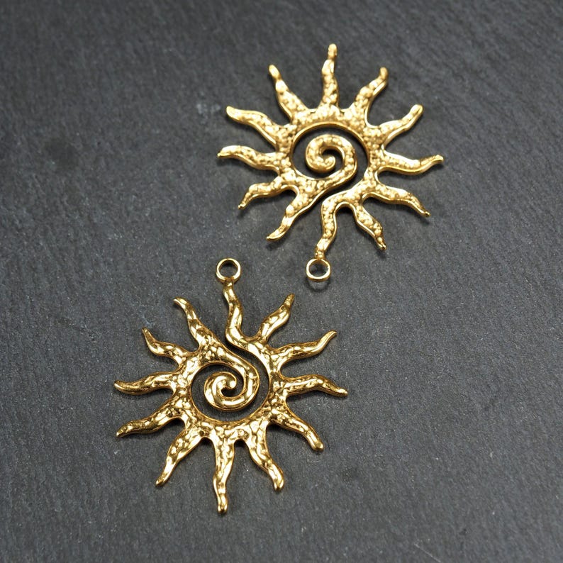 May include: Two gold-toned metal sun charms with a spiral design in the center. Each charm has a loop at the top for attaching to jewelry or other crafts.