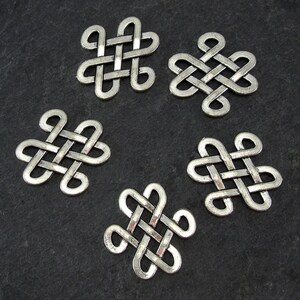 Puede incluir: Cinco amuletos de nudo celta de metal plateado, cada uno con forma cuadrada y un diseño de nudo intrincado.