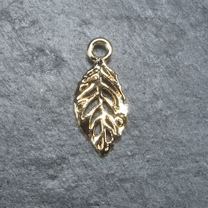 May include: Gold-toned metal leaf charm with a delicate, intricate design. The charm has a loop at the top for attaching to jewelry or other crafts.
