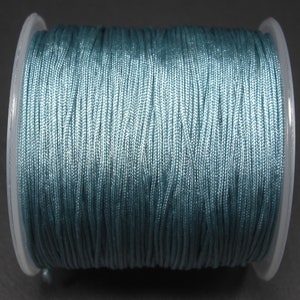 May include: A spool of teal-colored cord, tightly wound and ready for use. The cord appears to be made of a smooth, synthetic material, ideal for crafting or jewelry making. The spool is made of clear plastic.