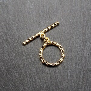 May include: Gold-toned metal toggle clasp with a round, textured ring. The clasp is a popular jewellery making component.