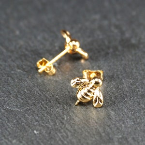 May include: A pair of gold bee stud earrings. The bee is detailed with a textured body and wings.