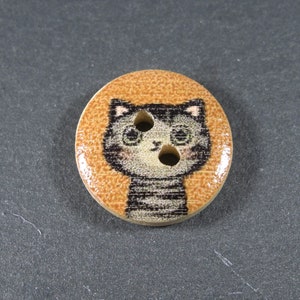 Puede incluir: Un bot&oacute;n de madera con fondo marr&oacute;n y un gato de dibujos animados en blanco y negro con un patr&oacute;n a rayas. El gato tiene dos ojos negros y una nariz rosa.