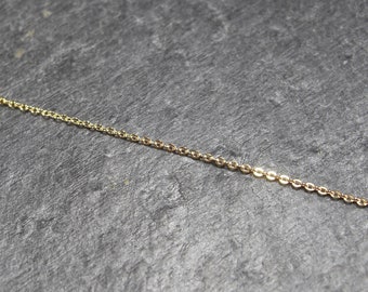 May include: A close-up of a gold chain necklace on a gray background.