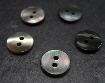 Puede incluir: Cuatro botones de dos agujeros hechos de nácar iridiscente. Dos botones son negros y dos son de un color iridiscente claro.