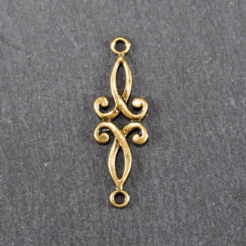 Puede incluir: Conector de metal dorado con un dise&ntilde;o decorativo y adornado. El conector tiene dos bucles en la parte superior e inferior.