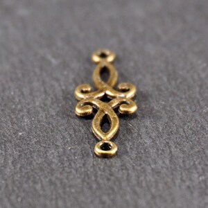 Puede incluir: Un conector de metal dorado con un dise&ntilde;o decorativo y ornamentado. El conector tiene dos bucles en la parte superior e inferior, lo que lo hace ideal para la elaboraci&oacute;n de joyas u otros proyectos de artesan&iacute;a.