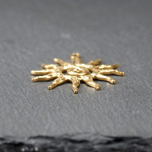 May include: A gold-toned sun pendant with a textured surface and a spiral design in the center.