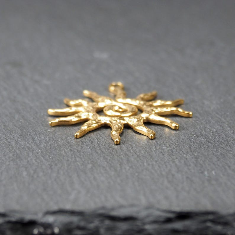 May include: A gold-toned sun pendant with a textured surface and a spiral design in the center.