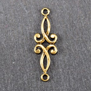 Puede incluir: Pendiente de metal dorado con un dise&ntilde;o decorativo y ornamentado. El pendiente tiene dos bucles en la parte superior e inferior para sujetarlo a joyas.