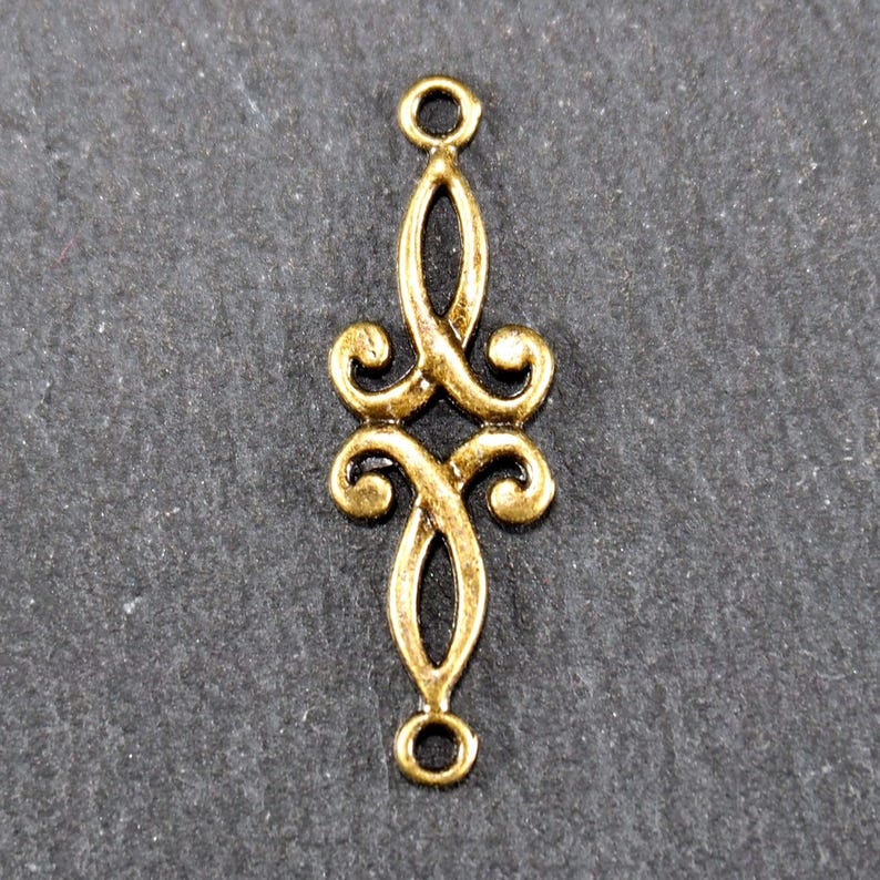 Puede incluir: Pendiente de metal dorado con un dise&ntilde;o decorativo y ornamentado. El pendiente tiene dos bucles en la parte superior e inferior para sujetarlo a joyas.