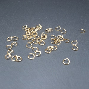 May include: A scattering of gold jump rings on a dark grey surface. The rings are small and delicate, perfect for jewellery making.