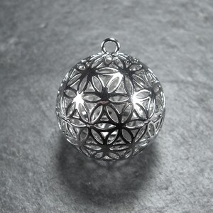 May include: Silver pendant featuring a geometric flower of life design. The pendant is hollow and has a loop at the top for attaching a chain.