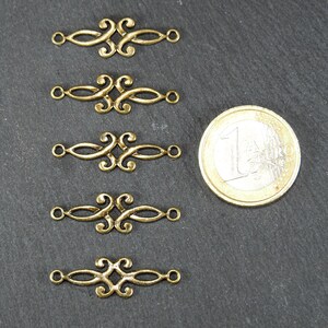 Puede incluir: Cinco piezas de conexi&oacute;n de metal dorado con un dise&ntilde;o decorativo y ornamentado. Cada pieza tiene dos bucles en cada extremo. Las piezas est&aacute;n dispuestas en una fila vertical, con una moneda de euro para la escala.