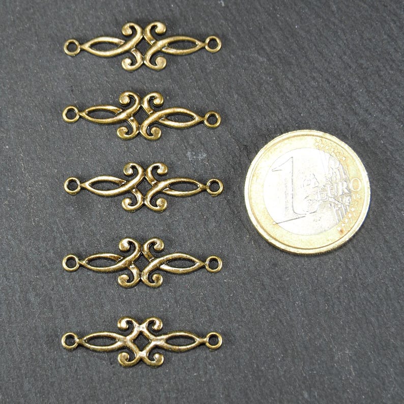 Puede incluir: Cinco piezas de conexi&oacute;n de metal dorado con un dise&ntilde;o decorativo y ornamentado. Cada pieza tiene dos bucles en cada extremo. Las piezas est&aacute;n dispuestas en una fila vertical, con una moneda de euro para la escala.