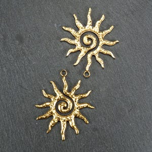 May include: Two gold-toned metal sunburst charms with a spiral design in the center. The charms have a hammered texture and are perfect for jewelry making.